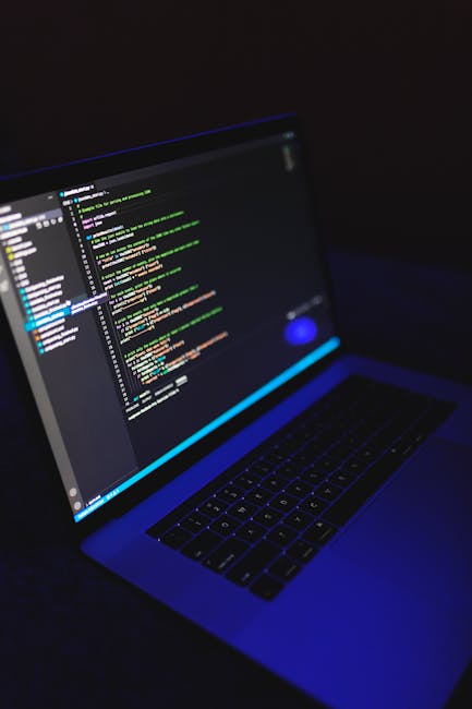 A close-up view of a modern laptop with a backlit keyboard, displaying lines of colorful code on its high-resolution screen. The background is dark, emphasizing the vibrant colors of the coding text, 